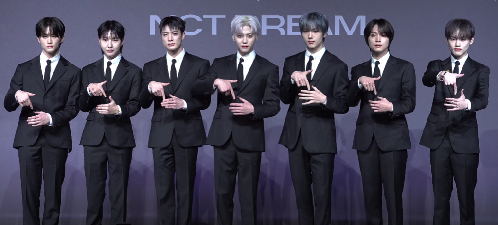 NCT DREAM members standing together at the DREAM()SCAPE press conference, posing for media photos in formal stage outfits.